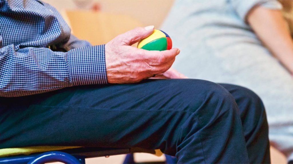 person-holding-multicolored-ball-339619 Elderly man holding a colorful therapy ball indoors, promoting relaxation and health.